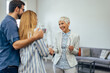 © bnenin - A smiling woman dressed in a suit, holding glasses, shaking hands with a young couple.