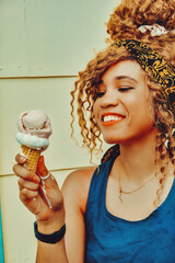 young adult woman afro hair smiling eating ice cream outdoors summertime looking away shot