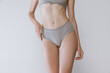 Cropped image of slender female body, belly and buttocks in underwear isolated over grey studio background