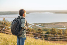 Tourist With Backpack Standing On Top Of Hill In Grass Field And Enjoying Beautiful Landscape View. Rear View Of Teenage Boy Hiker Resting In Nature. Active Lifestyle. Concept Of Local Travel