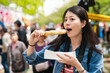 © PR Image Factory - cheerful asian girl holding and eating oden on stick with tourists on background while taking cherry blossom viewing trip in the mint museum in Osaka, japan at springtime
