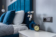 Analog clock alarm clock on the nightstand by the bed against the background of pillows