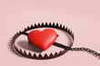 Red heart placed in a rusty trap on white background to illustrate Internet love scam or online romantic swindle.