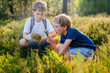 © Iryna - Two children boys with backpack looking examining moss through magnifying glass while exploring forest nature and environment on sunny day during outdoor ecology school less.