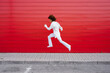 © VISTA by Westend61 - Cheerful young woman jumping over sidewalk by red wall