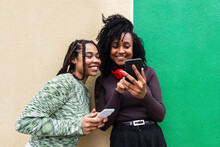 Happy Multiracial Friends With Mobile Phones Standing In Front Of Wall