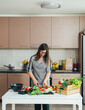 © Tijana - Beautiful Woman in Apron Cutting Organic Pepper on a Cutting Board at Kitchen Table