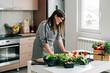 © Tijana - Smiling Woman Reading Recipe on a Digital Tablet while Cooking Lunch in the Modern Kitchen