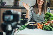 © Tijana - An Anonymous Woman Holding Lettuce While Sitting At Kitchen Desk And Filming Video For Her Food Channel