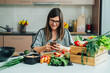 © Tijana - Happy Woman Using Mobile Phone while Making Healthy Lunch in the Kitchen