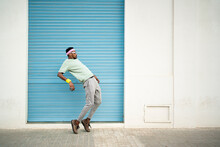 Flexible Young Man Dancing On Footpath In Front Of Blue Shutter