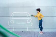Young woman rechsrging painted car with green plug