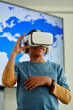 © Seventyfour - Vertical portrait of young black boy using VR in school classroom with geography map in background