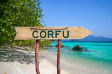 Corfu Wooden Arrow Road Sign Against Beach With White Sand And Turquoise Water Background. Travel To Greece Concept.