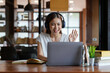 © Natee Meepian - Online education. A female student with headphones learning online at home, she waving hand to other students or colleagues on computer monitor in video conference and smiling.