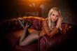 Beautiful blonde model with perfect legs in pantyhose posing on the red sofa in a leather jacket