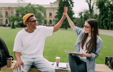 Two young people are studying together near university. Students outdoors giving five to each other.