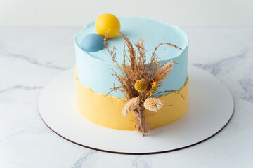 Canvas Print - Birthday cake with yellow and blue cream cheese frosting decorated with dried field flowers on the white background