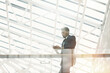 © Mediaphotos - Serious fashionable young black businessman leaning on railing and texting message while waiting for colleague in business lobby