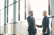 © Mediaphotos - Smiling confident young black manager with beard standing in lobby and shaking hand of senior business partner while welcoming him