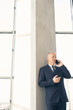 © Mediaphotos - Content handsome mature businessman in formal suit leaning on column in lobby while talking by cellphone