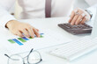 © Mediaphotos - Close-up of unrecognizable male financier sitting at workplace and using calculator and graph paper while calculating profit of company