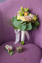 Wedding rings and a bridal bouquet on a purple chair.