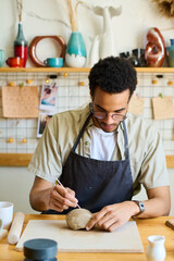 Aufkleber - Young craftsman with sharp handtool cutting piece of clay into two parts on square board while creating new handmade items for sale