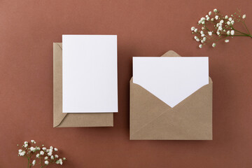 Wall Mural - Blank greeting cards and envelopes with dry flowers on brown background. Blank paper sheet cards with mockup copy space. Minimal workplace composition. Flat lay, top view