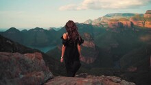 Young woman in black dress enjoying the view of a valley during sunset, huge canyon landscape visible in background.