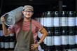 © เลิศลักษณ์ ทิพชัย - Male brewer carrying metal beer kegs at brewery Small Business and the Beer Industry A smiling handsome young man in an apron holds a steel beer keg on his shoulder in a warehouse.