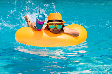 Child in swim pool swimming on inflatable ring. Kid swim with orange float. Water toy, healthy outdoor sport activity for children. Kids beach fun. Fashion summer kids hat.