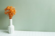 Vase of orange gypsophila flowers on white table. khaki green wall background