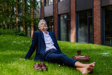 Mature businessman resting and sitting barefoot in park, feeling free, escaping from work, work life balance concept.