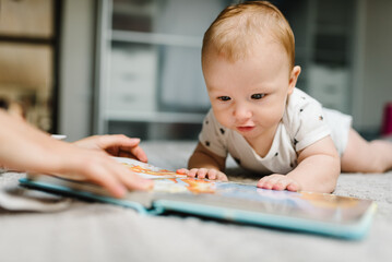 Portrait of mother and baby boy read book in bed at home. Mom with son.