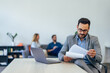 © bnenin - Focused man checking some documents, reading them while colleagues sitting in the background.