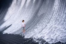 A Boy In Denim Shorts And A White T-shirt Looks At An Artificial Waterfall.