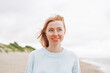 © Galina Zhigalova - Portrait of young red haired woman in light blue sweater on sand beach by sea in storm