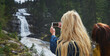 Woman photographing a waterfall on her cellphone during a hike in nature with a friend.Two women on a hike in nature together taking a photo of a waterfall using a cellphone.