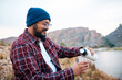 © Meeko Media - An adult man pours coffee on hiking trip in the mountains with lake view