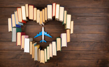 Education Abroad Creative Concept. Heart Shape Of Books And Airplane On The Wooden Desk. Love To Travel