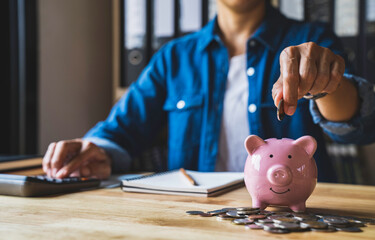 woman holds a coin in a pig-shaped piggy bank to save money for the future. after retirement and record keeping of income, expenditure, savings and financial concepts.