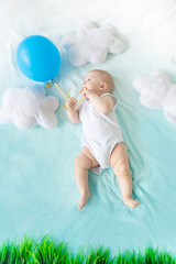 a baby with a balloon in his hand on a blue sky background with clouds, the concept of travel and summer holidays