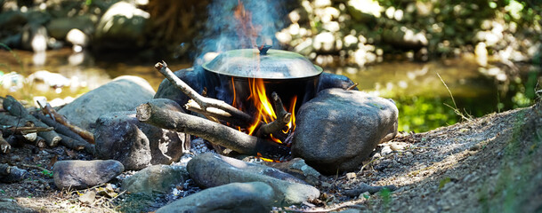 flames burning the pot, hearth with the pot on the river bank, picnic in the woods