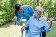 © supAVADEE BUTRADEE - young nurse caring for a senior man sitting on a wheelchair. Nurses take in the fresh air in the garden and raise their hands to encourage home care.