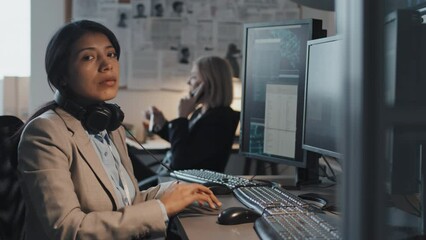 Waist up portrait of female Hispanic analyst taking off headset after using computer, doing research, sitting at desk in office, looking on camera