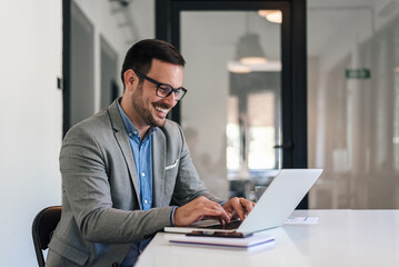 Wall Mural - cheerful male professional working on laptop while sitting at office desk