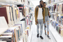 Happy College Student Couple At Bookshelf In Library