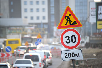 Roadworks warning traffic signs of construction work on city street and slowly moving cars