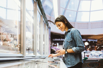 Wall Mural - Happy young woman shopping for groceries in supermarket